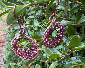 May include: A pair of copper wire earrings with a teardrop shape, each adorned with a cluster of small, dark red beads.