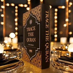 May include: A black book with gold lettering titled "Trace the Quran: Arabic Calligraphy" with a gold and black patterned design on the cover.