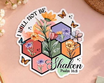 May include: A die-cut sticker featuring a honeycomb pattern with colorful floral illustrations inside each cell. The text reads I WILL NOT BE Shaken Psalm 16:8. Small butterflies and sparkles are scattered around the hexagonal floral arrangement.
