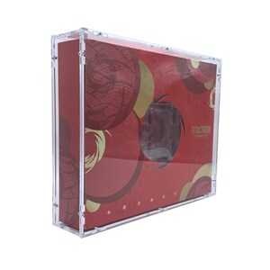 May include: A rectangular display case made of clear acrylic, housing a red box with gold and dark red circular patterns. The box features a central cutout window and printed text in a non-Latin script, secured by small metal screws at the corners.