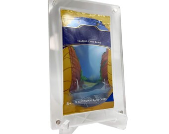 Op de afbeelding: Een transparante acryl display met een standaard, waarop een verzegeld boosterpack voor een verzamelkaartspel te zien is. Het pack heeft een blauw en gouden ontwerp met een berglandschap en de tekst "Trading Card Game".