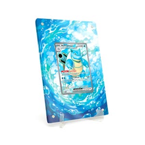 Könnte beinhalten: Eine gerahmte Pokémon-Karte mit dem Charakter Blastoise GX, vor einem blau-weißen Hintergrund mit Wasser-Motiv. Die Karte wird auf einem transparenten Acrylständer präsentiert, der das Design und die Details der Karte hervorhebt.