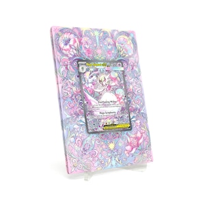 May include: A pastel-coloured card binder with a floral design and a Pokémon card. The binder features a pink, purple, and blue colour scheme with a decorative pattern. The Pokémon card is visible in the centre of the binder.