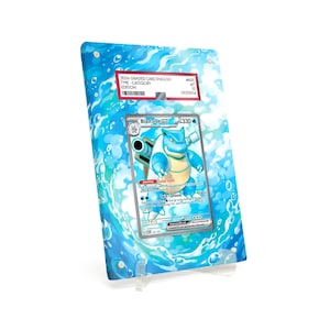 May include: A graded Pokémon card featuring Blastoise, displayed in a clear acrylic case. The case has a blue water-themed background. The card is labeled with the text "2036 GRADED CARD ENGLISH" and other details.