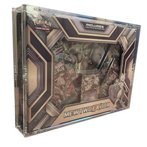 Puede incluir: Una vitrina de acrílico transparente que contiene una caja Mewtwo EX del juego de cartas coleccionables Pokémon. La caja presenta un diseño plateado y negro con el logotipo de Pokémon y el texto "MEWTWO EX BOX". Incluye una carta promocional Mewtwo-EX.