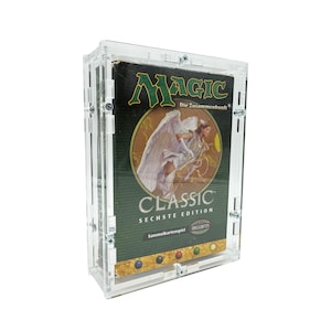 Puede incluir: Una caja de acrílico transparente con una caja de juego de cartas Magic: The Gathering Classic Sexta Edición en su interior. La caja tiene un fondo verde con un ángel blanco y el texto "Magic: The Gathering Die Zusammenkunft" y "Classic Sechste Edition".