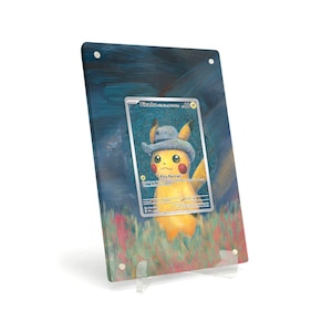 Könnte beinhalten: Gerahmtes Kunstwerk mit einer Pikachu-Sammelkarte. Die Karte zeigt Pikachu mit Hut vor einem farbenfrohen, impressionistischen Hintergrund. Das Kunstwerk wird auf einem transparenten Ständer präsentiert, der das Design der Karte hervorhebt.