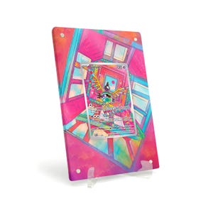 May include: A framed Sigilyph Pokémon card displayed on a clear stand. The card is centered on a vibrant, colorful background with geometric shapes and window-like designs. The card features a colorful illustration of the Pokémon Sigilyph.