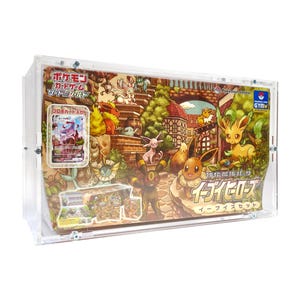 May include: A clear plastic display case containing a Pokemon card game. The case features a colourful illustration of Eevee and its evolutions in a whimsical setting. The text on the case reads "Pokemon Card Game, Eeveelutions, Eevees Set".
