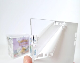 Op de afbeelding: Een transparante acryl display case met een beschermend folie die wordt verwijderd. De case is ontworpen om trading cards te bewaren en te presenteren.