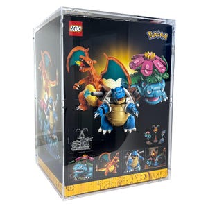 May include: A clear display case featuring a LEGO set with Pokémon characters. The set includes Charizard, Blastoise, and Venusaur figures. The LEGO logo and Pokémon branding are visible on the box. The background is black with illustrations of the characters.