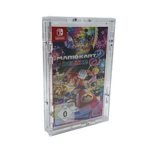 Puede incluir: Una caja de plástico transparente con un cartucho de juego de Nintendo Switch en su interior. El juego es Mario Kart 8 Deluxe. La caja tiene una clasificación USK de 0.