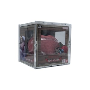 Puede incluir: Una vitrina de acrílico transparente con marco de estilo madera alberga un objeto rojo con forma de cerebro. La vitrina presenta gráficos y texto impresos, incluido el logotipo de Bandai Namco. El diseño sugiere un artículo de colección.