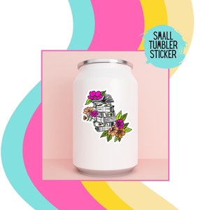 May include: A white tumbler with a sticker of a stack of books with flowers on top. The sticker is black and white with pink, orange, and yellow flowers. The text "SMALL TUMBLER STICKER" is in a white circle with a black outline.