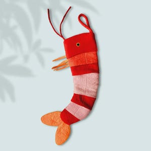 Peut inclure: Une chaussette de Noël fantaisiste en forme de crevette. La chaussette est principalement rouge avec des rayures roses et blanches, des accents orange et une boucle pour l'accrocher. Le design comprend des antennes et une queue, créant un look amusant et festif.
