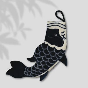 May include: A black and white fish-shaped stocking with a loop for hanging. The fish has a detailed scale pattern and a white belly. The design is reminiscent of Japanese carp streamers, often used for decoration.