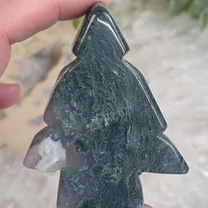 May include: A tree-shaped stone carving with a mix of green and white patterns. The stone has a polished surface and is held up by a hand. The carving is a decorative item, possibly for display or collection.