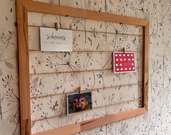 Op de afbeelding: Een houten displayframe met touwlijnen voor het ophangen van foto's en notities. Het frame bevat drie kaarten: één met tekst, één met schapenillustraties en een foto van een zeehond. De achtergrond is een behang met bloemenpatroon.