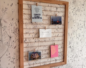 Op de afbeelding: Een houten fotolijst met een raster van touw, met verschillende kaarten en foto's. De kaarten hebben tekst in het Duits, waaronder "Nicht mein Problem" en "schoenes aus der Werkstatt".