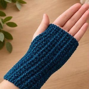 May include: A dark teal fingerless glove featuring a textured, ribbed crochet pattern. The accessory covers the wrist and the lower portion of the palm, showcasing a consistent, dense stitch construction throughout the entire piece.