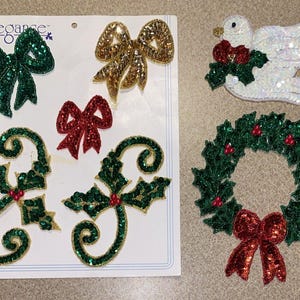 May include: A set of six decorative holiday-themed patches featuring sequined designs including a green bow, a gold bow, a red bow, two holly sprigs, a white dove with a red bow, and a green wreath with a red bow, all on a white backing card.