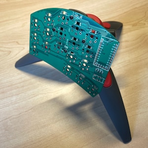 Puede incluir: Una placa de circuito verde con una fila de pines en el lado derecho, montada en un soporte negro y rojo.