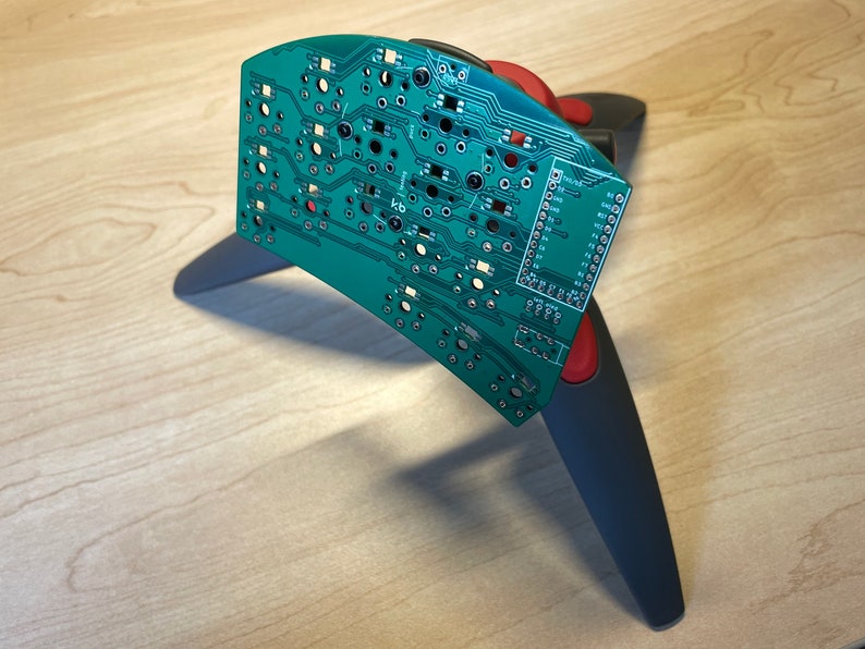 Puede incluir: Una placa de circuito verde con una fila de pines en el lado derecho, montada en un soporte negro y rojo.