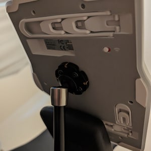 Puede incluir: Soporte de tableta blanco con un soporte giratorio negro y un brazo de metal negro. El soporte tiene un pestillo de pl&aacute;stico blanco en el lateral y una peque&ntilde;a luz roja en la parte posterior. El soporte est&aacute; unido a un brazo de metal negro que est&aacute; conectado a una base negra.