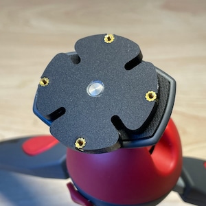 Puede incluir: Primer plano de una cabeza de tr&iacute;pode negra con una placa en forma de estrella de cinco puntas. La placa tiene cinco tornillos dorados alrededor del borde.