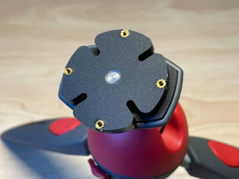 Puede incluir: Primer plano de una cabeza de tr&iacute;pode negra con una placa en forma de estrella de cinco puntas. La placa tiene cinco tornillos dorados alrededor del borde.