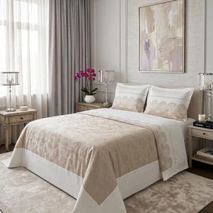Può includere: Una camera da letto lussuosa con un letto con copriletto beige e bianco e federe abbinate. La stanza comprende comodini con lampade, un tappeto e un dipinto. L'ambiente è caratterizzato da una palette di colori neutri.