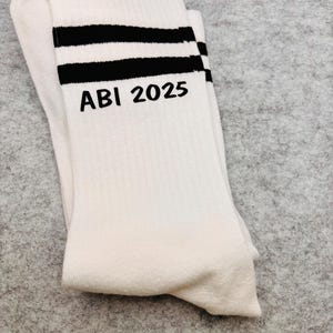 May include: White socks with two black stripes and the text "ABI 2025" embroidered on the front.