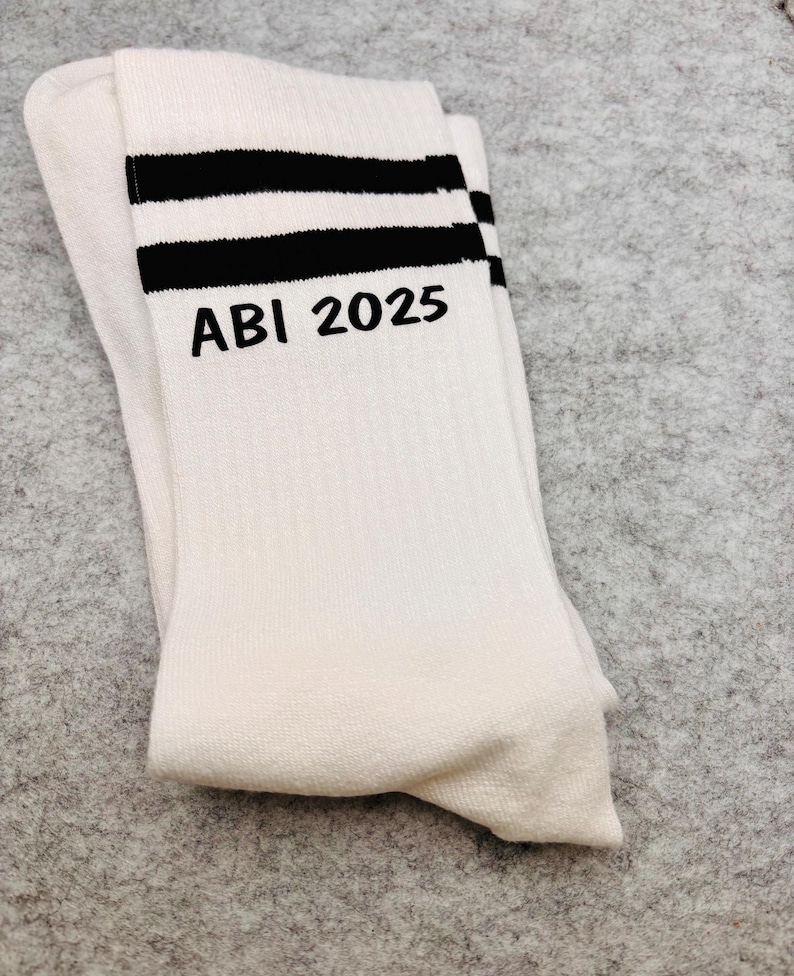 May include: White socks with two black stripes and the text "ABI 2025" embroidered on the front.