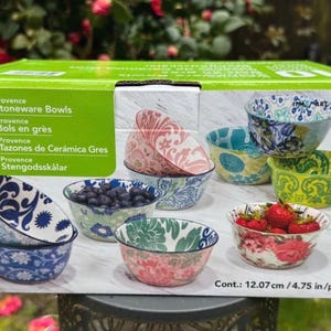 May include: A set of 10 Provence stoneware bowls. The bowls display floral patterns in blue, green, pink, and yellow. Each bowl has a diameter of 12.07 cm. The box has text in multiple languages.