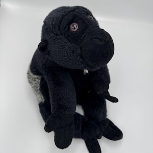 Puede incluir: Un peluche de gorila negro con una mancha gris en la espalda. El gorila tiene cara, orejas y manos negras, con ojos rosas. El juguete está diseñado para ser suave y tierno.