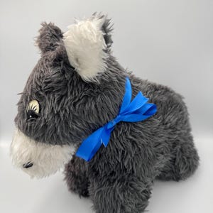 Może przedstawiać: Pluszowa zabawka w kształcie psa w kolorze szarym i białym z niebieską kokardką. Pies ma białą twarz i białe uszy.