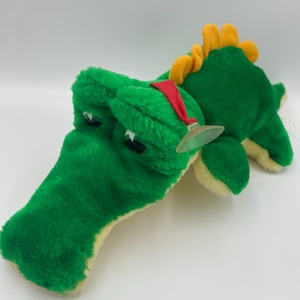 Op de afbeelding: Groen pluche alligator speelgoed met een gele stekelige rug en een rode bandana. De alligator heeft zwarte ogen en een witte buik.