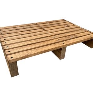 May include: A small, rectangular wooden pallet with a natural finish. The pallet is constructed with horizontal wooden slats secured by small black nails. It has three supporting legs and is suitable for various display or decorative purposes.