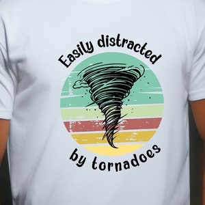May include: White t-shirt with a vintage-style graphic of a tornado. The text reads "Easily distracted by tornadoes".