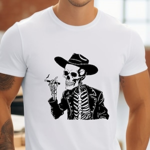 May include: White t-shirt featuring a black and white graphic of a skeleton wearing a cowboy hat and leather jacket, holding a cigar. The skeleton design is detailed and stylized.
