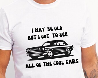 May include: White t-shirt with a black graphic of a classic car and the text "I may be old but I got to see all of the cool cars".