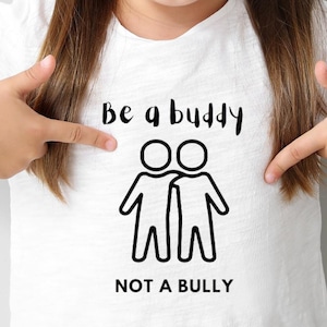 May include: White t-shirt with black text that reads "Be a buddy not a bully". The text is accompanied by a simple black line drawing of two stick figures holding hands.