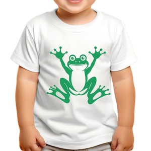 May include: White t-shirt featuring a large green frog graphic. The frog is depicted with its arms and legs outstretched, giving a playful appearance. The design is centered on the shirt, making it a fun and eye-catching piece of apparel.