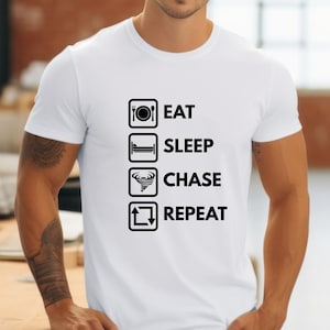 Könnte beinhalten: Weißes T-Shirt mit einer schwarzen Grafik, auf der "Essen, Schlafen, Jagen, Wiederholen" steht, mit Symbolen, die jedes Wort repräsentieren.