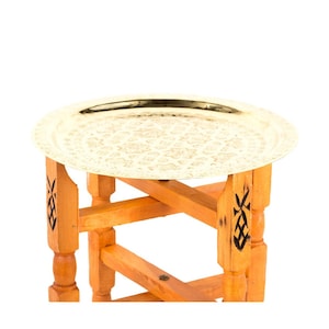 Peut inclure: Un plateau rond doré avec un motif floral en relief repose sur une table en bois. La table a une finition en bois naturel avec des accents décoratifs noirs sur les pieds. Le plateau est idéal pour servir ou exposer, environ 40 cm de diamètre.