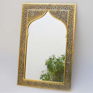 Op de afbeelding: Een gouden spiegel met een sierlijk, gegraveerd frame. Het frame heeft een traditioneel boogontwerp met ingewikkelde bloemmotieven.