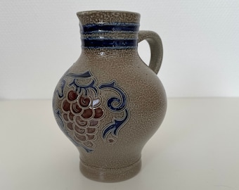 May include: A small, gray ceramic pitcher with a blue and white stripe around the top and a grape design on the front.