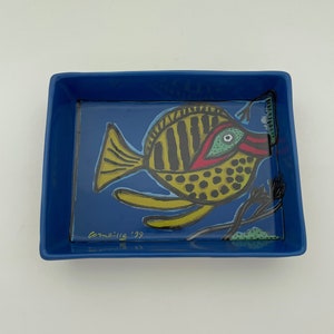 Può includere: Un vassoio in ceramica blu con un design di pesce colorato. Il pesce è giallo, nero, rosso e verde. Il vassoio è firmato "Corneille '99".