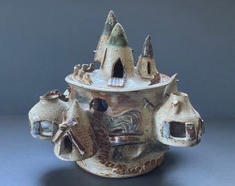 Könnte beinhalten: Eine Keramikskulptur eines fantasievollen Schlosses mit mehreren Türmen und Fenstern. Das Schloss ist mit braunem, weißem und grünem Glasur verziert und hat eine strukturierte Oberfläche.
