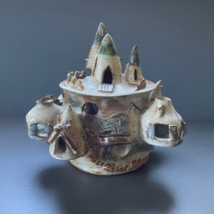 Op de afbeelding: Een keramische sculptuur van een fantasievol kasteel met meerdere torens en ramen. Het kasteel is versierd met bruine, witte en groene glazuur en heeft een getextureerd oppervlak.